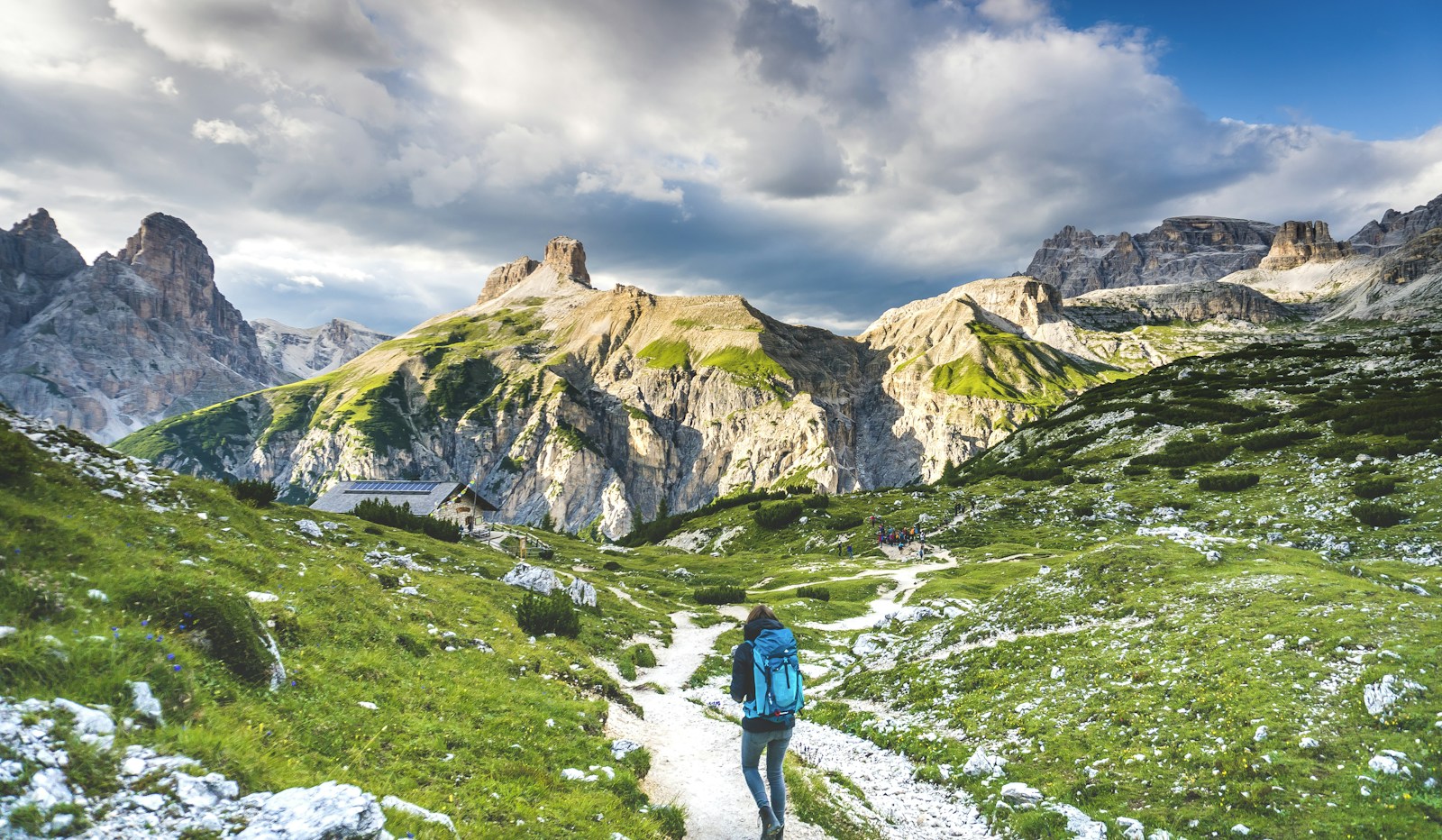 A hiker following a trail beneath the dramatic peaks of the Dolomites