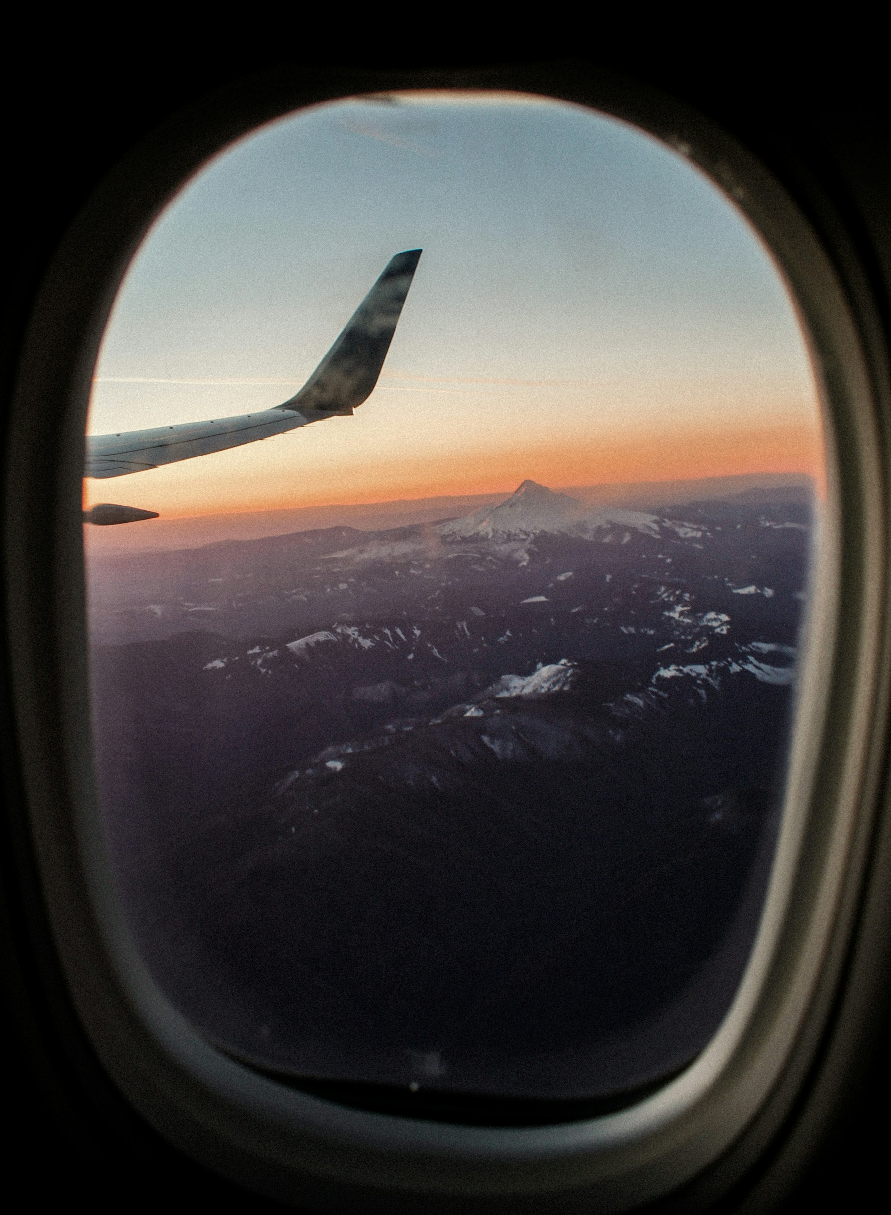 Airplane window overlooking mountain peaks at sunset