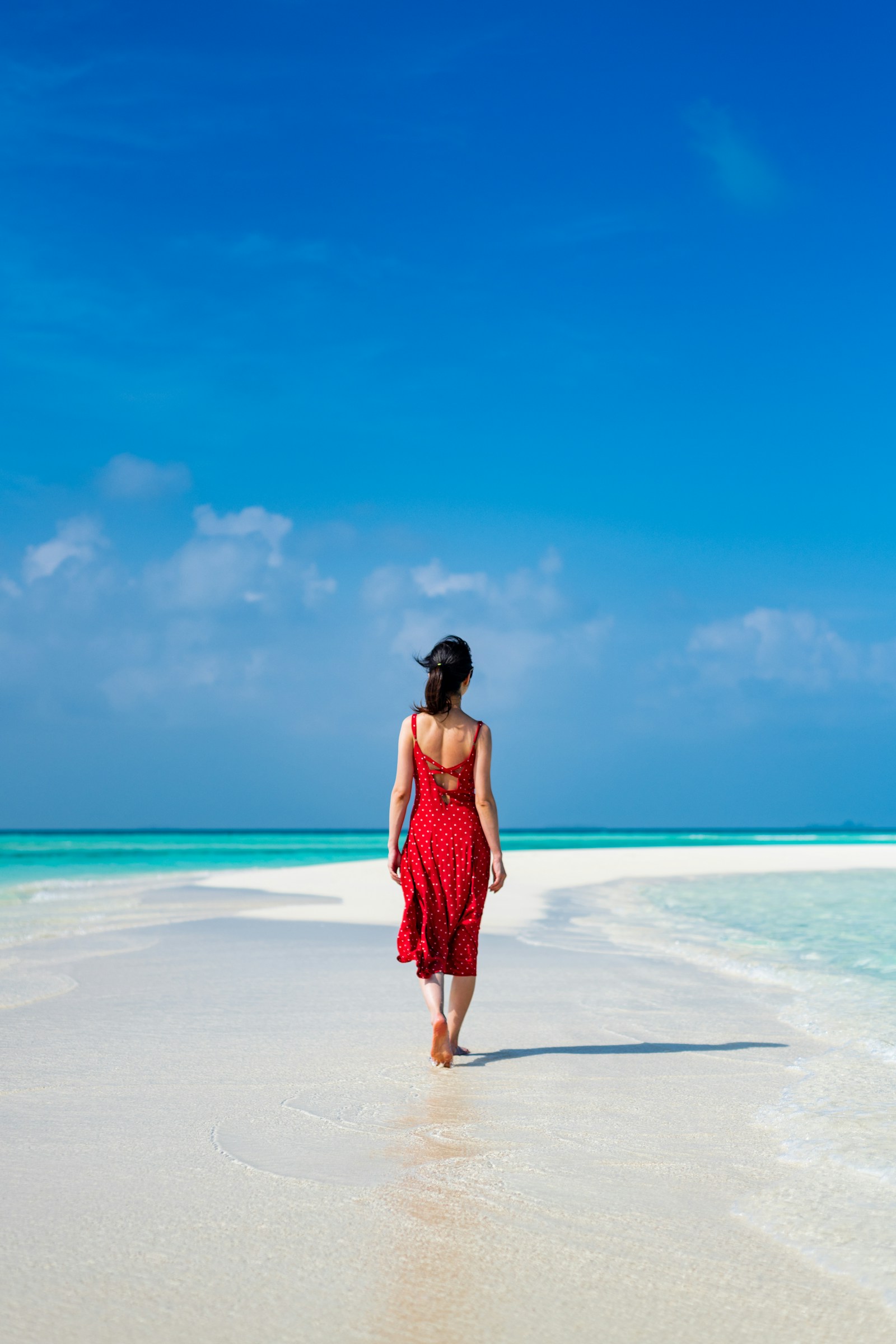 A traveller in a red dress walking beside turquoise sea on a sunny beach